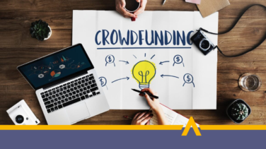 Plansza z napisem crowdfunding obok laptop i aparat