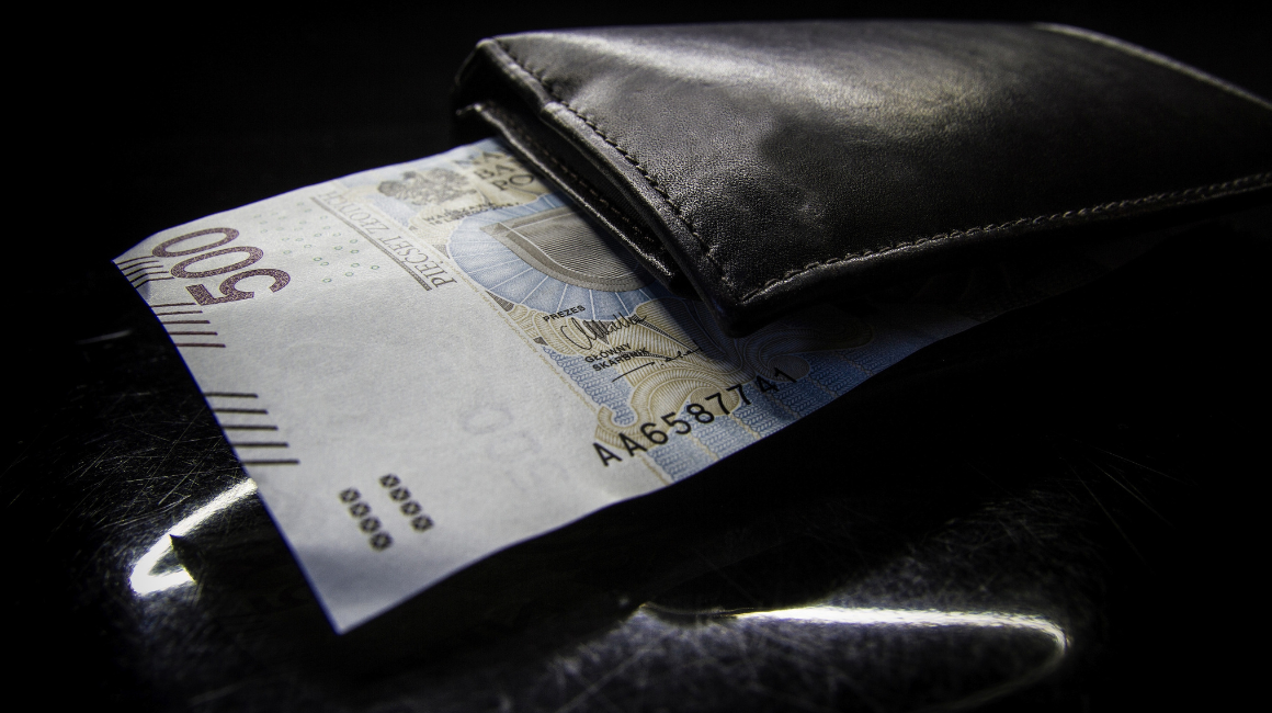 Banknot 500 złotych częściowo wysunięty z czarnego skórzanego portfela na ciemnym tle